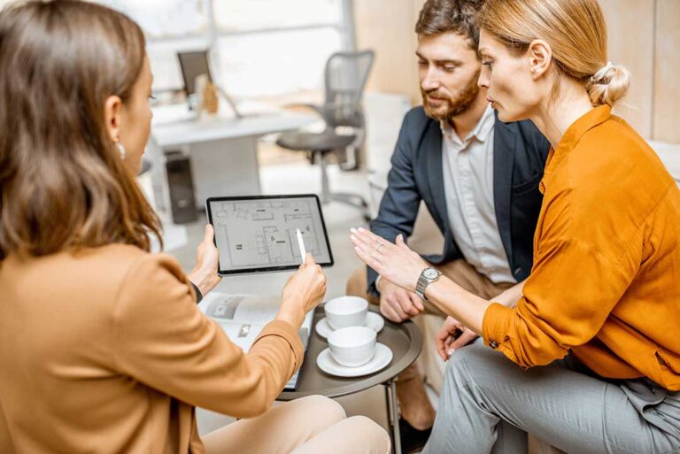 Homebuyers and an escrow officer reviewing closing documents at a table with paperwork and pens visible.