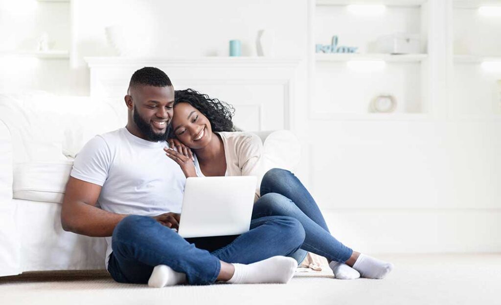 A young couple reviews home inspection documents at a kitchen table inside an unfurnished house.