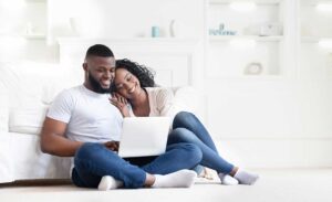 A young couple reviews home inspection documents at a kitchen table inside an unfurnished house.